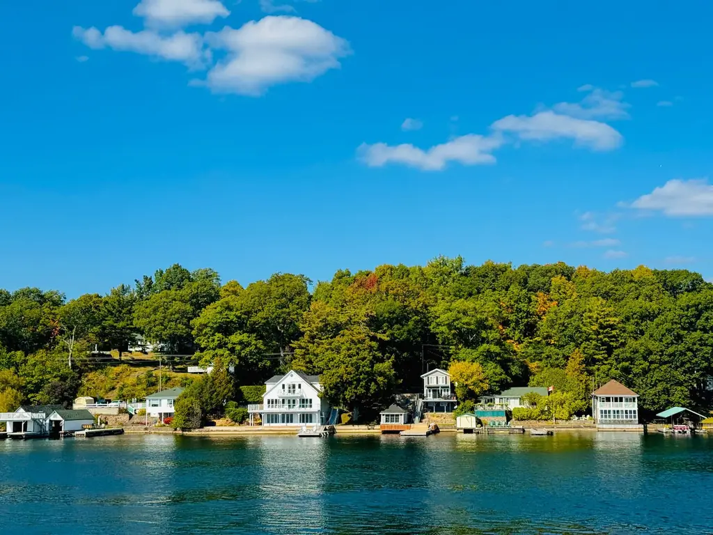 Lakefront scene with cottages and lush green forest under a blue sky in Leeds and the Thousand Islands