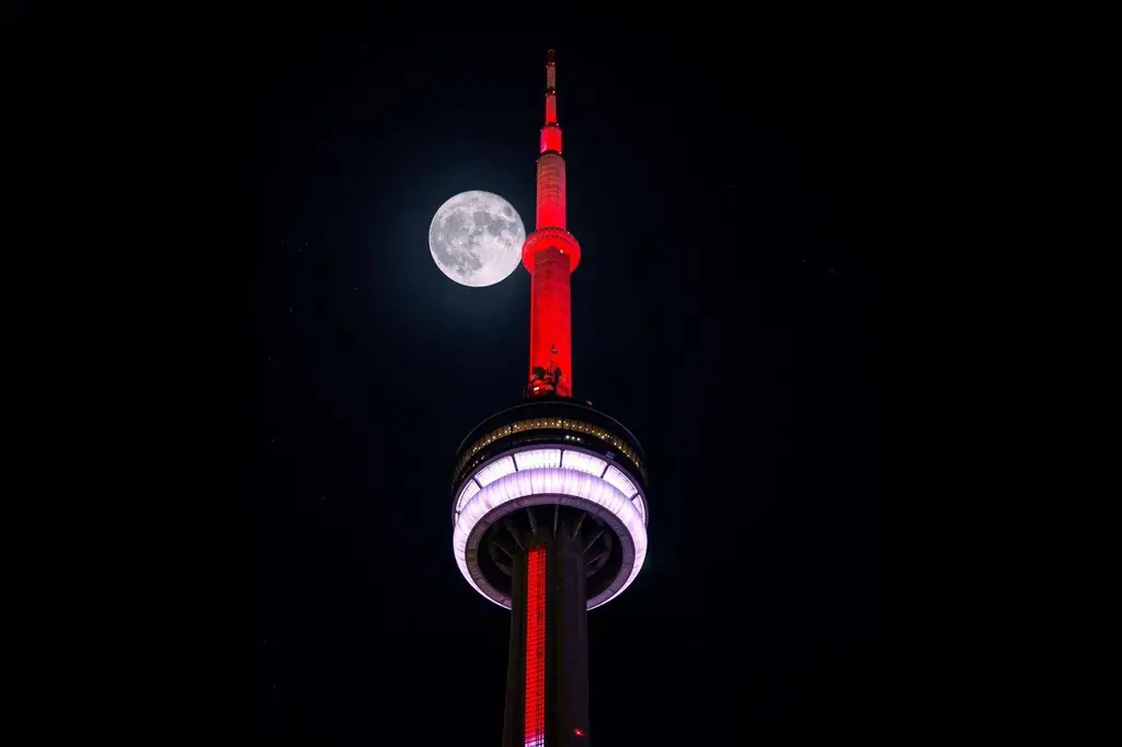 CN Tower lit up in red with a full moon in Toronto's night sky