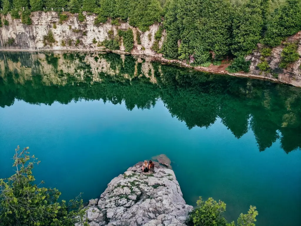 Aerial shot of people sitting on rock by Elora Quarry, Canada reflecting trees and cliff