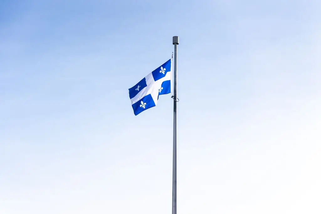 Quebec flag waving on a flagpole against a clear blue sky, symbolizing pride and identity