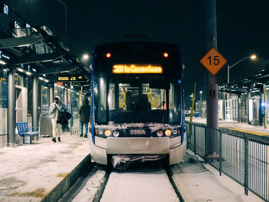 Snow-covered light rail station at night in Kitchener, Ontario with passengers boarding