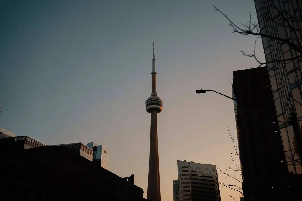 The CN Tower in Toronto silhouetted against a dusky sky, surrounded by modern buildings