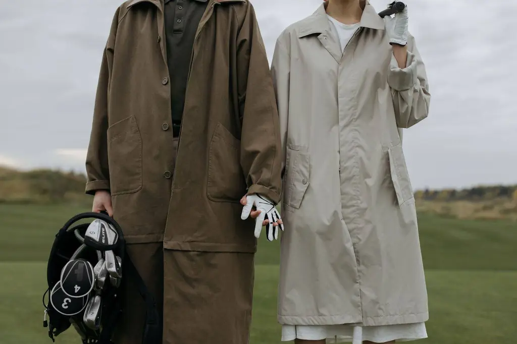 Couple standing on a golf course holding hands and golf bag, wearing long coats