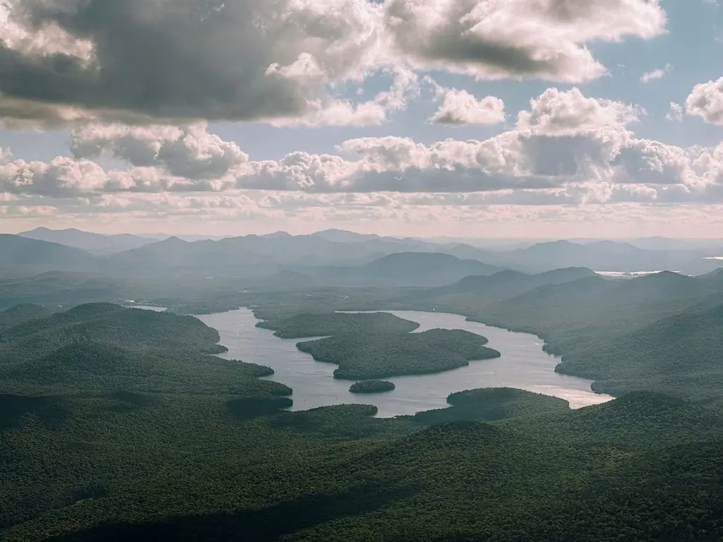 Aerial landscape of the Adirondack Mountains with winding river, clouds, and sunlight