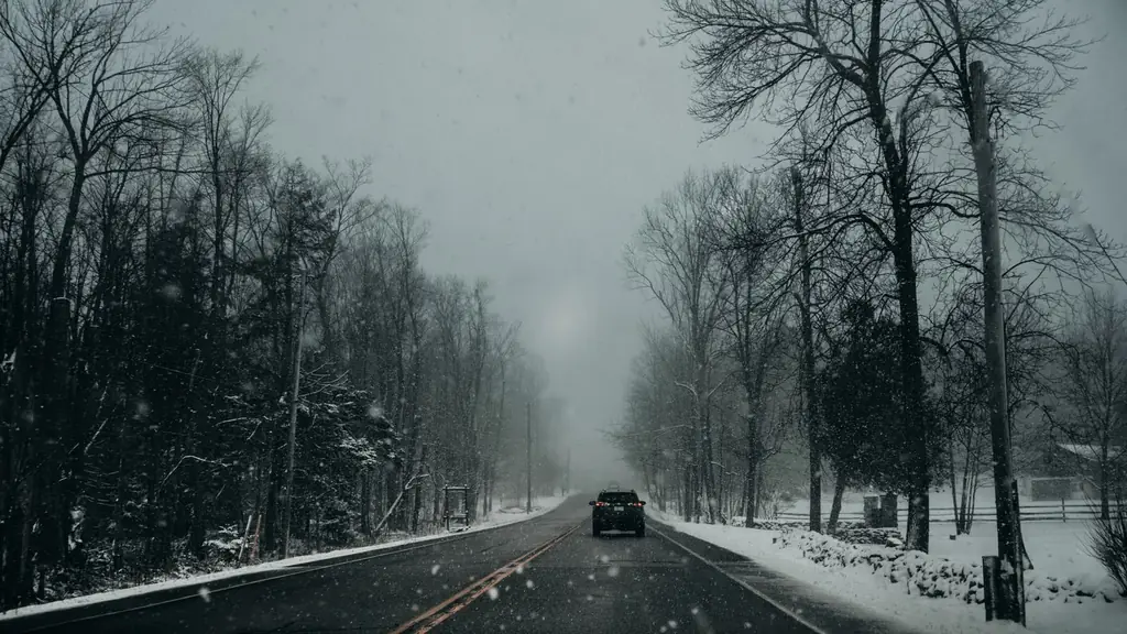 A lone car travels a snow-covered road through a barren winter landscape in Kitchener, Ontario