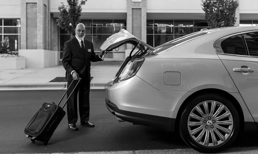 Chauffeur in suit loading luggage into luxury car trunk outside a modern building