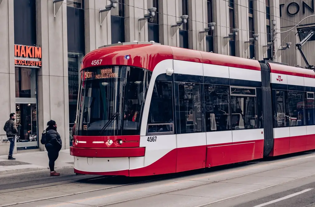Red streetcar on city street with passengers and buildings in background