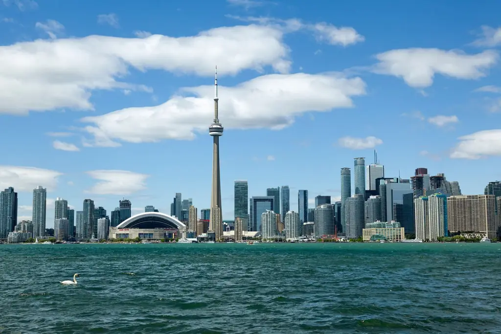 View of Toronto's skyline featuring the iconic CN Tower, with waterfront reflections on a summer day