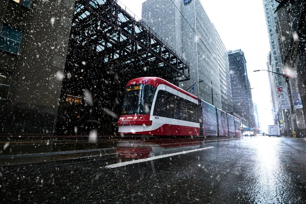 A Toronto streetcar navigating a snowy city street during winter with downtown buildings