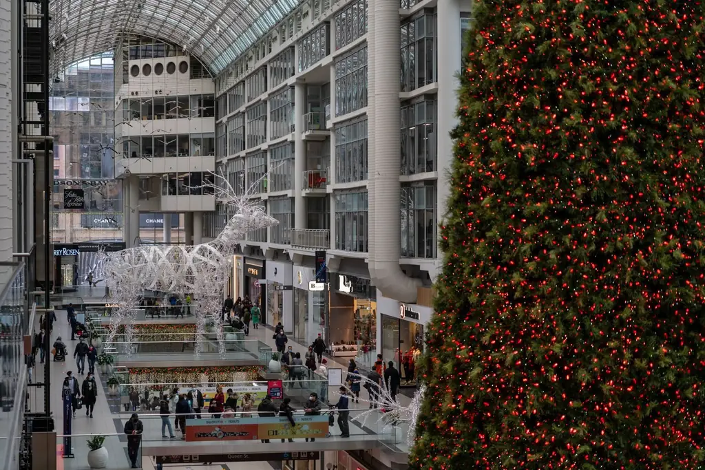 People shopping amidst festive decorations, including a large Christmas tree, inside a Toronto mall