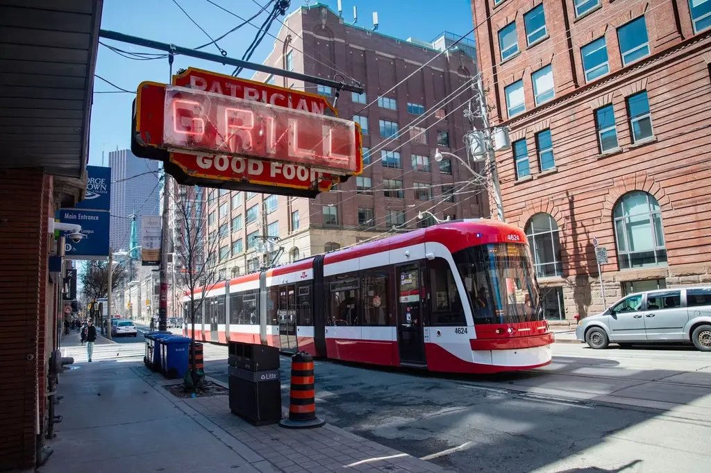A modern streetcar travels through Toronto's urban landscape under a vintage Patrician Grill sign