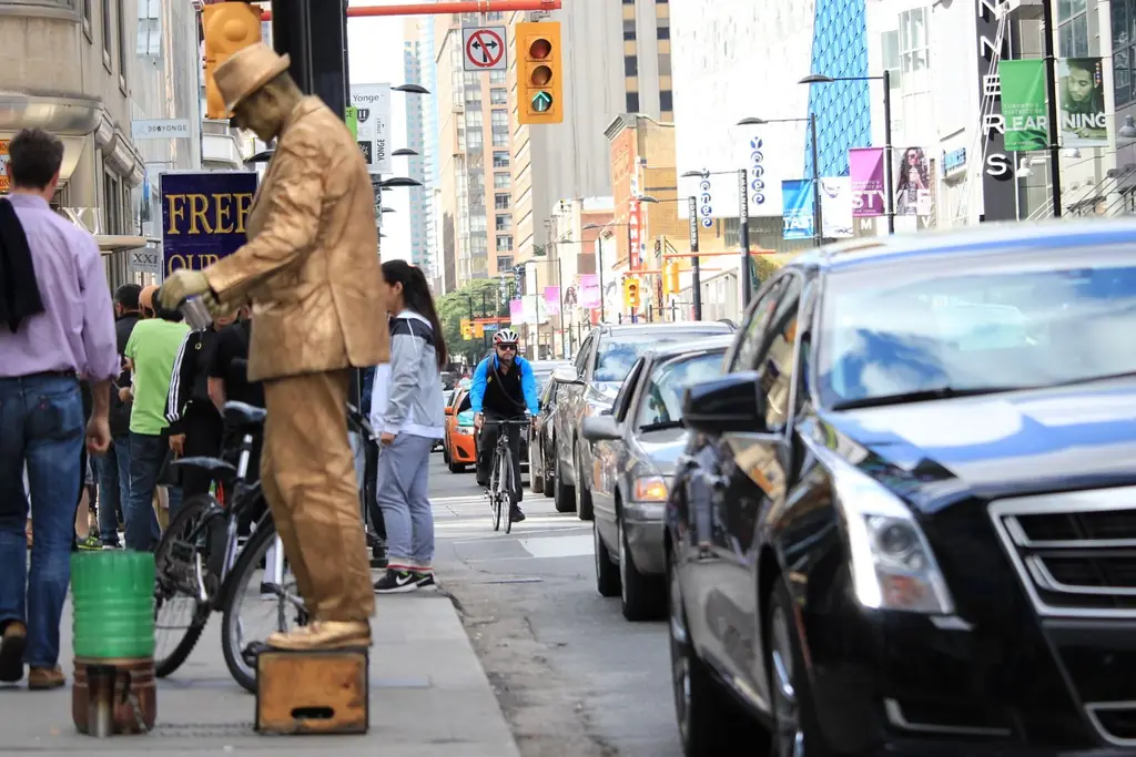 A bustling urban scene in Toronto featuring cars, a cyclist, and a street performer