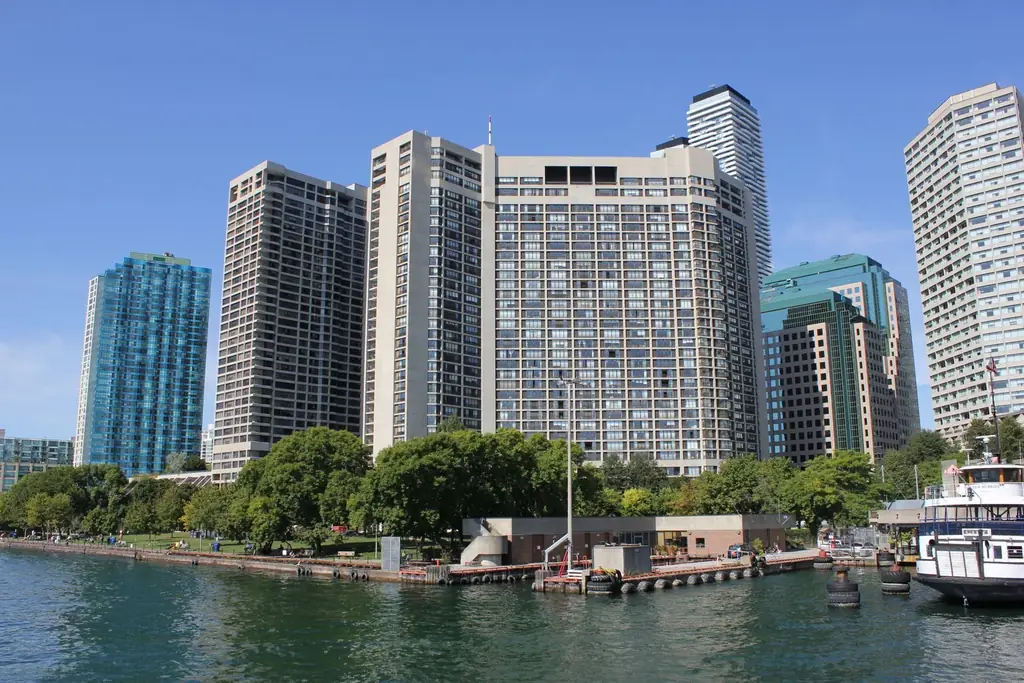 City skyscrapers rise above the waterfront with trees and a clear sky