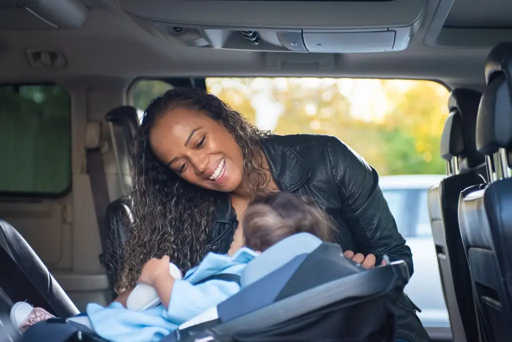 A joyful mother smiles at her baby in a car seat inside a vehicle