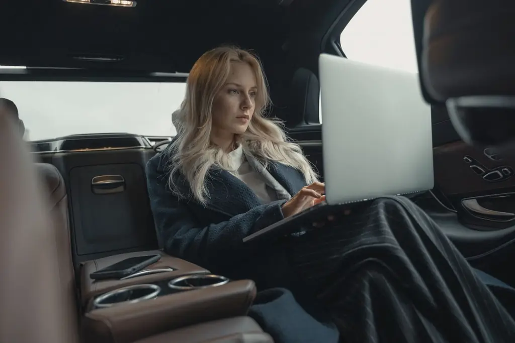 Businesswoman working on her laptop in the back seat of a luxury car