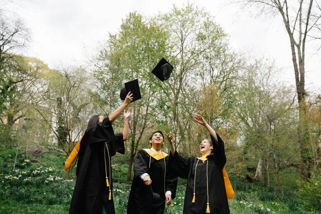 Three graduates celebrating and throwing caps in the air in a lush green park