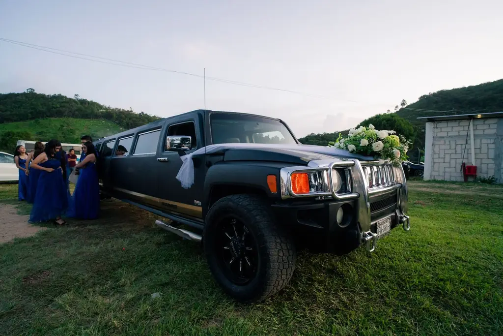 Black limousine adorned with floral wedding decorations parked outdoors with people in the background