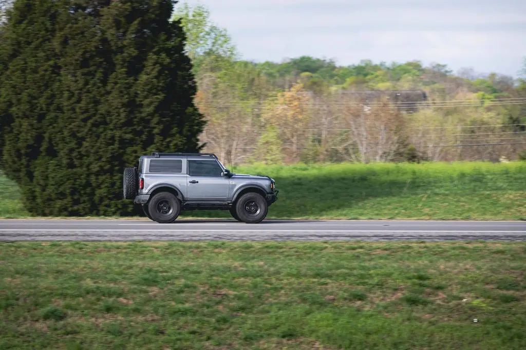 A silver SUV speeds along a scenic rural highway amidst lush greenery on a clear day